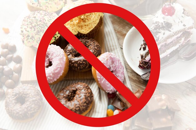 comida rápida, dieta baja en carbohidratos, engorde y concepto de alimentación poco saludable - cierre de donuts glaseados, pasteles y dulces de chocolate detrás de ningún símbolo o signo de prohibición de barra diagonal inversa