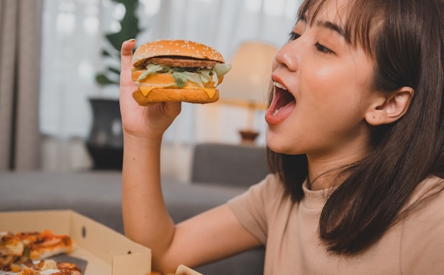 Comida rápida para llevar en casa. Comer hamburguesa a la hora de llevar y entregar. Estilo de vida de la mujer asiática en la sala de estar. Distanciamiento social y nueva normalidad.