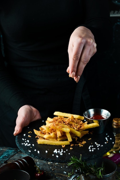 Comida rápida, papas fritas. Patatas con tocino en un plato en manos de un chef, sobre un fondo rústico de madera. Concepto de comida rápida.