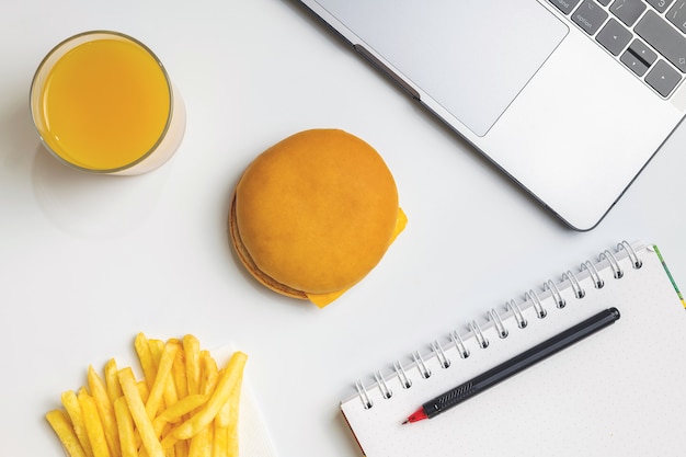 Comida rápida en el trabajo de merienda. Ordenador portátil, hamburguesa y papas fritas en el lugar de trabajo.
