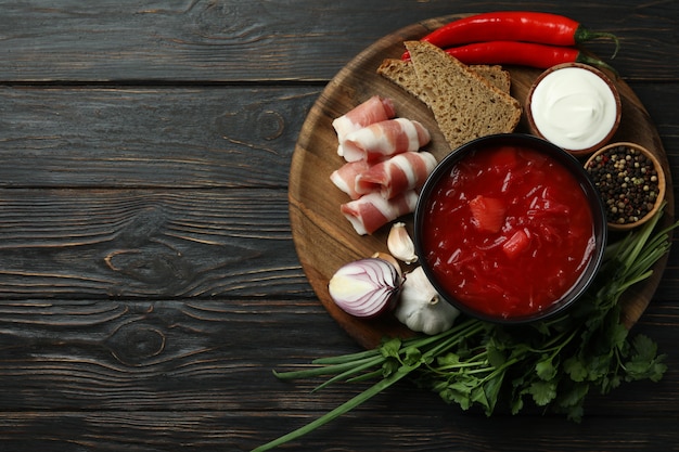 Comida sabrosa con borscht e ingredientes sobre superficie de madera