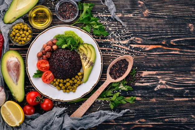 Comida saludable Arroz negro aguacate tomates cherry guisantes y avellanas Sobre un fondo de madera Vista superior Espacio libre para el texto