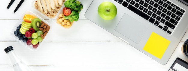 Comida saludable en caja de comida en mesa de trabajo con laptop