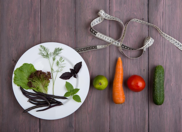 Comida saludable y dieta concepto vegetariano cinta métrica plato blanco con hoja de ensalada pepino tomate y otras verduras