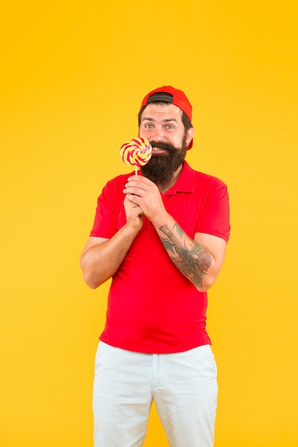 La comida saludable es una dieta de vida saludable y calorías Hombre con piruleta y sonrisa brutal hombre en uniforme se preocupa por una sonrisa saludable sabor dulce Hombre come piruleta grande y colorida feliz hipster ama la comida dulce