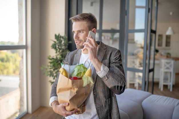 Comida saludable. Un hombre sosteniendo un paquete de anuncios de verduras hablando por teléfono.