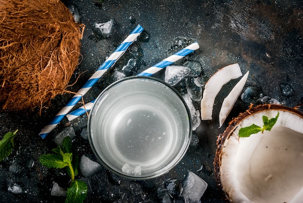 Comida sana . Agua de coco orgánico fresco con cocos, cubitos de hielo y menta, en azul oscuro oxidado, vista superior