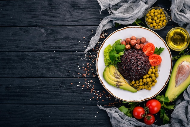 Comida sana. Arroz negro, aguacate, tomates cherry, guisantes verdes y avellana. Sobre un fondo de madera. Vista superior. Espacio libre para su texto.