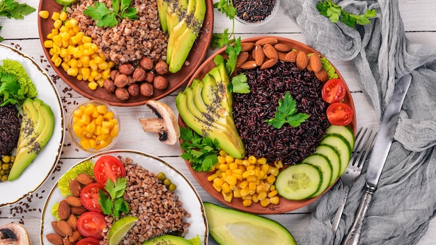 Comida sana. Arroz negro, trigo sarraceno, aguacate, tomates cherry, guisantes y avellana. Sobre un fondo de madera. Vista superior. Espacio libre para su texto.