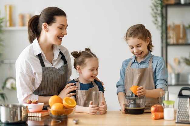 Comida sana en casa. Familia feliz en la cocina. Las hijas de la madre y de los niños están preparando zumo de naranja natural.