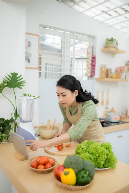 Comida sana, concepto de dieta. Mujer asiática cocinando ensalada de verduras para la cena, cortando tomates maduros en una tabla de cortar de madera en la cocina de casa.