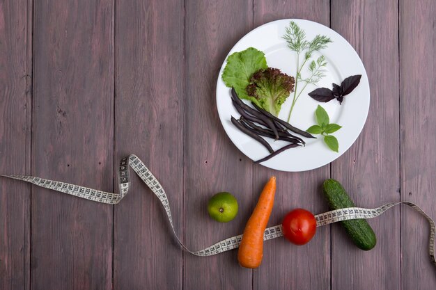 Comida sana y dieta concepto vegetariano cinta métrica plato blanco con hojas de ensalada de verduras