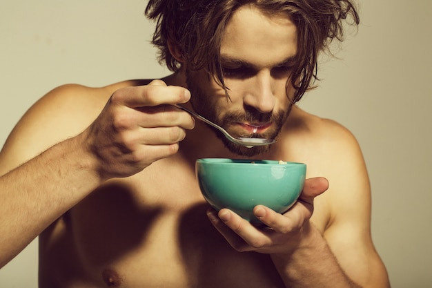 Comida sana y dieta, fitness, mañana. Hombre con el pecho desnudo desayunando avena con leche
