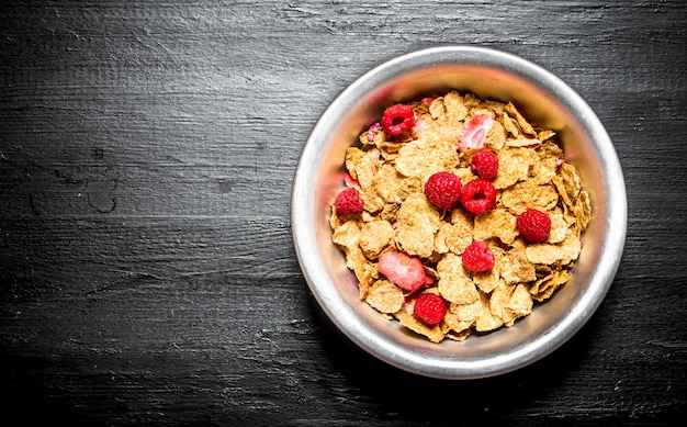 Comida sana. Muesli con frambuesas sobre mesa de madera negra.