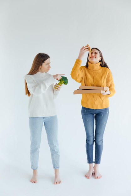 Comida sana. Una mujer sostiene una pizza y la otra un brócoli.