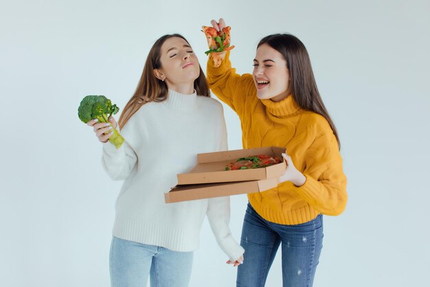 Comida sana. Una mujer sostiene una pizza y la otra un brócoli.