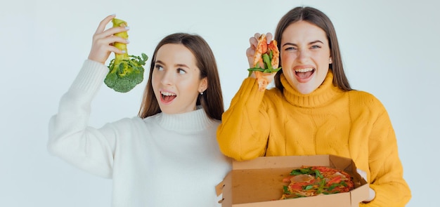 Comida sana. Una mujer sostiene una pizza y la otra un brócoli.