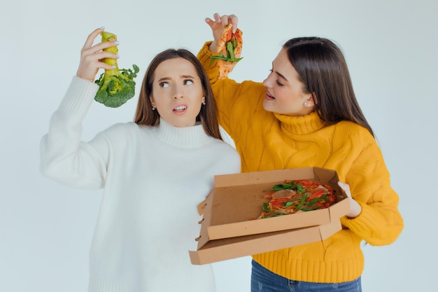 Comida sana. Una mujer sostiene una pizza y la otra un brócoli.