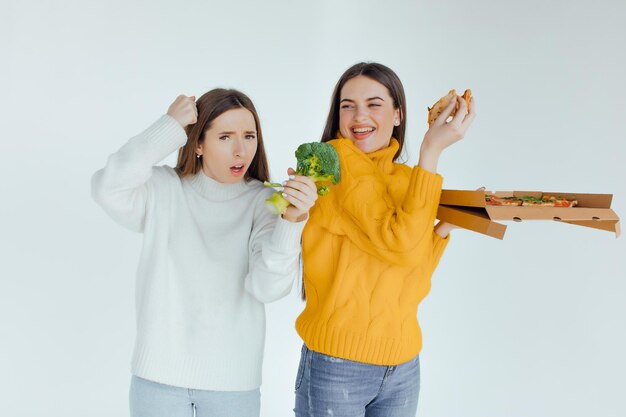 Foto comida sana. una mujer sostiene una pizza y la otra un brócoli.