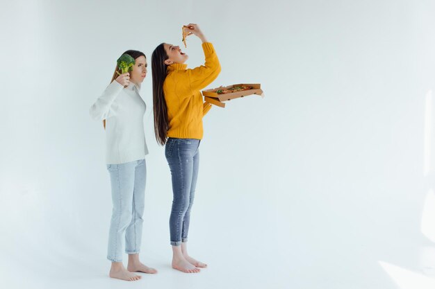 Comida sana. Una mujer sostiene una pizza y la otra un brócoli.