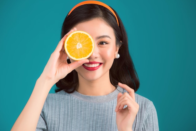 Comida sana Sonriente encantadora chica asiática pinup sosteniendo naranja sobre fondo azul