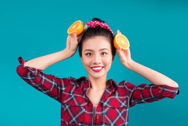 Comida sana. Sonriente a hermosa chica asiática pinup sosteniendo naranja sobre fondo azul.