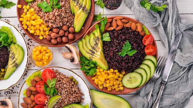 Comida saudável. Arroz preto, trigo sarraceno, abacate, tomate cereja, ervilhas verdes e avelã. Em um fundo de madeira. Vista do topo. Espaço livre para o seu texto.