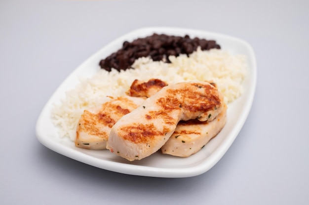 Comida saudável com peito de frango feijão e arroz em um prato branco