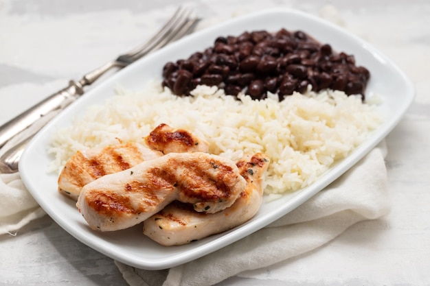 Comida saudável com peito de frango feijão e arroz em um prato branco