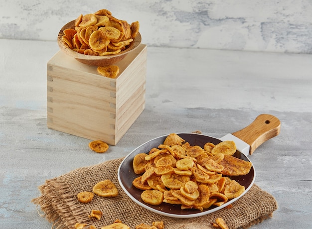 Comida saudável de chips de banana, frutas secas e chips de vegetais saudáveis, lanches vegan saudáveis na serapilheira em um prato e carrinho de madeira.