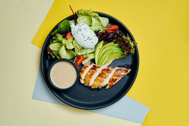 Comida saudável e dietética - filé de frango assado com alface e ovo escalfado em um prato de cerâmico preto na superfície colorida Vista superior