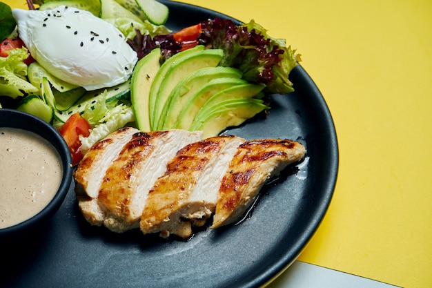 Comida saudável e dietética - filé de frango assado com alface e ovo escalfado em um prato de cerâmico preto na superfície colorida Vista superior