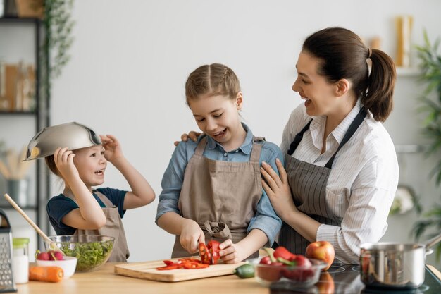 Comida saudável em casa. Família feliz na cozinha. Filhas de mãe e filhos estão preparando legumes.