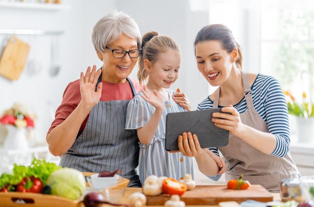 Comida saudável em casa. Família feliz na cozinha. Vovó, mãe e filha estão preparando legumes.