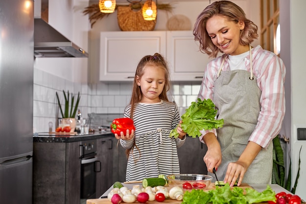 Comida saudável em casa. feliz família caucasiana na cozinha, mãe e filha estão preparando a refeição para o jantar