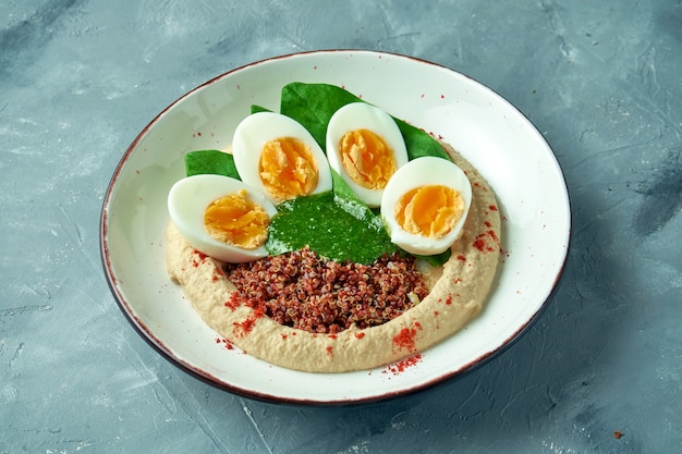 Comida saudável - homus com quinua, espinafre e ovo cozido em uma tigela branca sobre um cinza