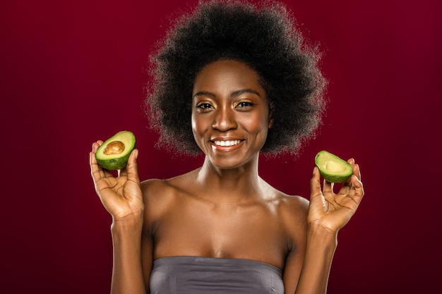 Comida saudável. Mulher simpática e positiva sorrindo para você enquanto segura duas metades de abacate