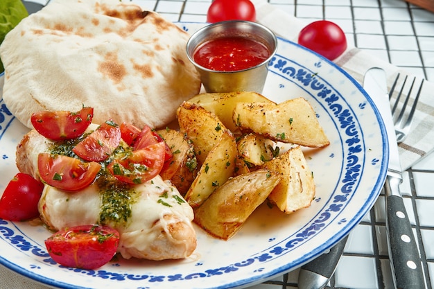 Comida saudável para o almoço: batata assada com filé de frango com mussarela e tomate cereja em um prato de cerâmico em uma mesa branca. Vista de perto