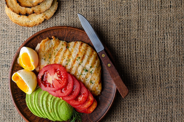 Comida saudável peito de frango grelhado com abacate, tomate, torrada e ovo cozido. postura plana, copyspace