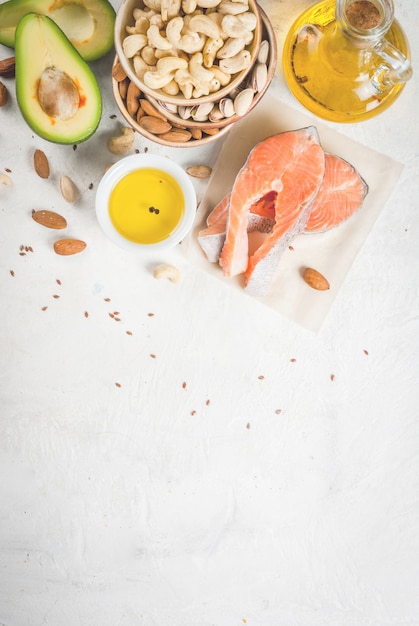 Comida saudável. Produtos com gorduras saudáveis. Omega 3, ômega 6. Ingredientes e produtos: truta (salmão), óleo de linhaça, abacate, amêndoas, castanha de caju, pistache. Em uma mesa de pedra branca. vista superior copyspace