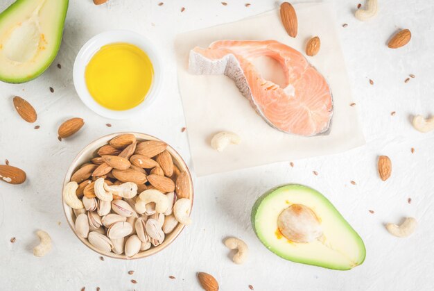 Comida saudável. Produtos com gorduras saudáveis. Omega 3, ômega 6. Ingredientes e produtos: truta (salmão), óleo de linhaça, abacate, amêndoas, castanha de caju, pistache. Em uma mesa de pedra branca. Vista superior do espaço da cópia