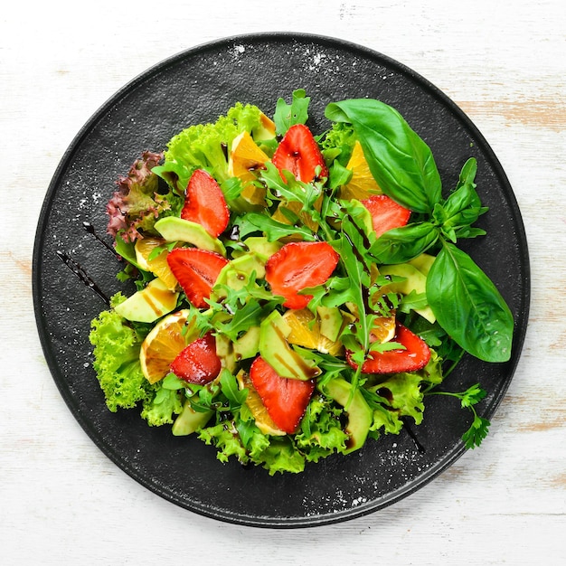 Comida saudável: salada de rúcula, abacate, morango e laranja. Vista do topo. Espaço livre para o seu texto.