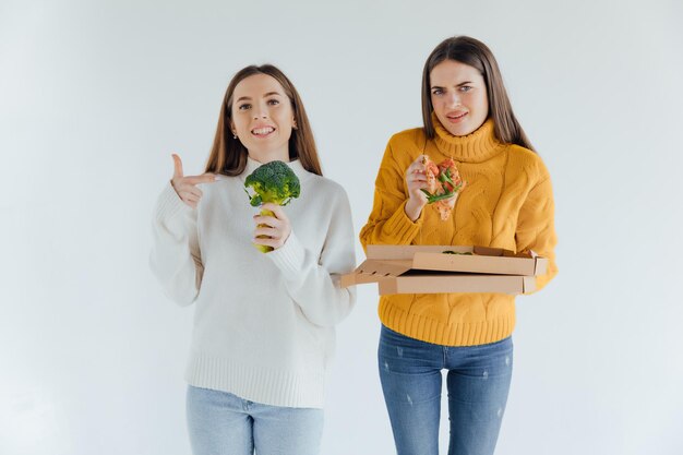 Comida saudável. Uma mulher está segurando uma pizza e a outra um brócolis