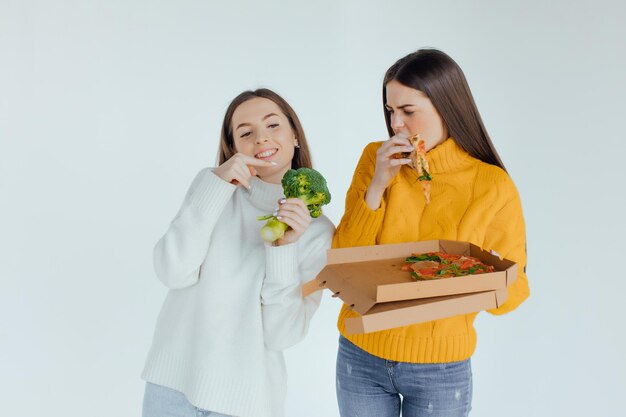 Comida saudável. Uma mulher está segurando uma pizza e a outra um brócolis