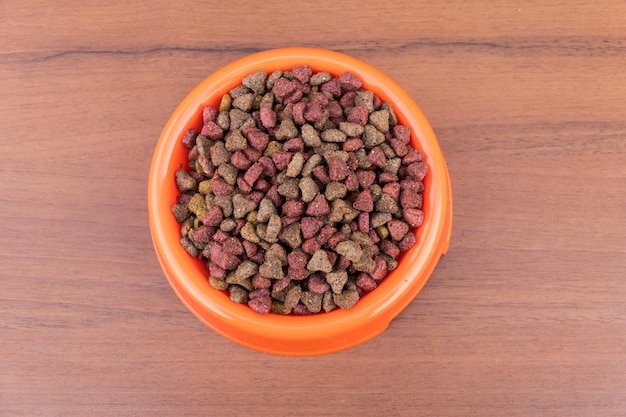 Comida seca para gatos en un tazón sobre fondo de madera. Alimentos para mascotas en la superficie de la madera. Vista superior