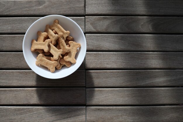 Comida seca para perros en un recipiente sobre fondo de madera vista superior.