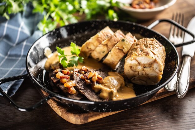 Comida Svieckova com bolinhos, molho e carne servida em prato escuro. Comida típica checa.