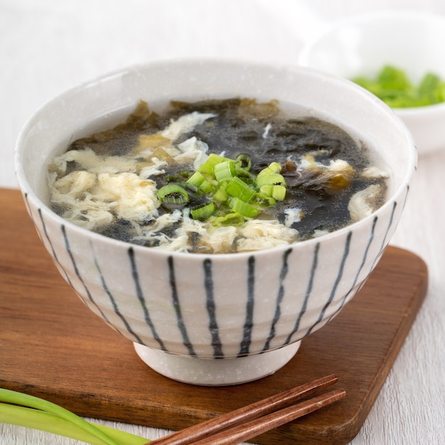 Comida taiwanesa: deliciosa sopa casera de huevo de algas marinas en un recipiente en una bandeja para servir sobre fondo de mesa de madera clara.