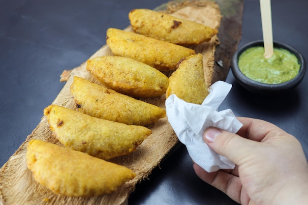 Comida típica colombiana milho empanada com molho picante em um tronco de madeira e uma empanada na mão