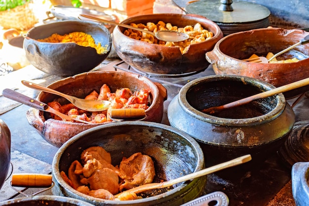 Comida tradicional brasileira sendo preparada em vasos de barro e no antigo e popular fogão de madeira